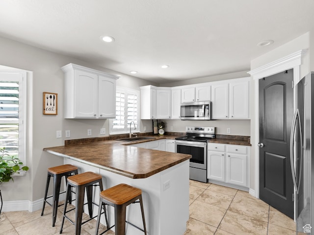 7341 W Sycamore Farm Rd, West Jordan, UT 84081 - kitchen featuring stainless steel appliances, dark countertops, a peninsula, white cabinetry, and a breakfast bar area