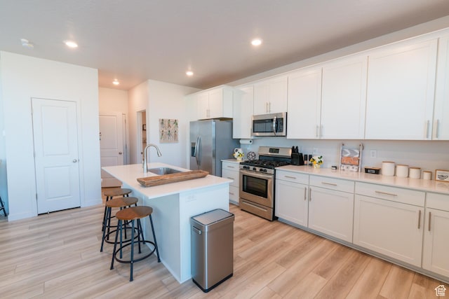 2006 N Red Yearling Dr, Saratoga Springs, UT 84045 - kitchen featuring stainless steel appliances, light wood-type flooring, a breakfast bar area, an island with sink, and white cabinets