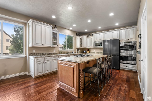14346 S Fort Duchesne Cv, Herriman, UT 84096 - kitchen featuring stainless steel appliances, glass insert cabinets, a center island, a kitchen breakfast bar, and dark wood-style floors