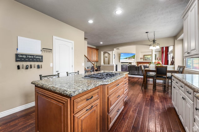 14346 S Fort Duchesne Cv, Herriman, UT 84096 - kitchen featuring arched walkways, stainless steel gas stovetop, decorative columns, dark wood-type flooring, and light stone countertops