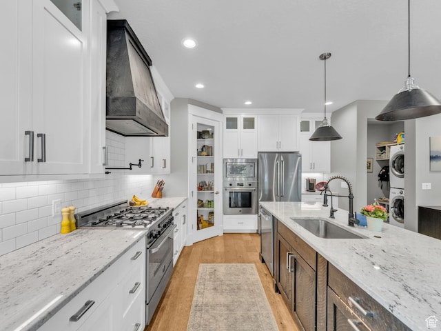 485 Parkview Dr, Summit Park, UT 84098 - kitchen featuring appliances with stainless steel finishes, estacked washer and dryer, custom exhaust hood, light wood-style floors, and glass insert cabinets