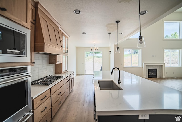7169 W Moorepark Pl, West Jordan, UT 84081 - kitchen featuring appliances with stainless steel finishes, light wood-style floors, custom exhaust hood, brown cabinets, and a chandelier
