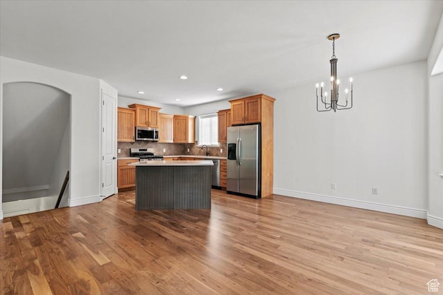 1076 W River Hill Dr, Spanish Fork, UT 84660 - kitchen featuring appliances with stainless steel finishes, a chandelier, light wood-style flooring, a kitchen island, and decorative backsplash