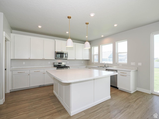 928 E Blackfeet Dr, Eagle Mountain, UT 84005 - kitchen featuring stainless steel appliances, light wood finished floors, white cabinets, a kitchen island, and light countertops