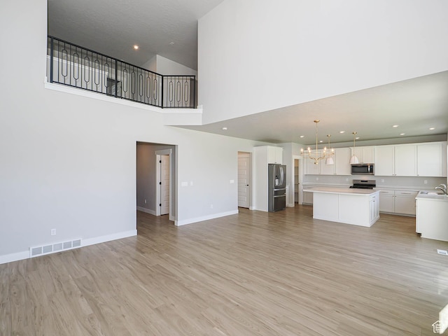 928 E Blackfeet Dr, Eagle Mountain, UT 84005 - unfurnished living room with a chandelier, light wood-style floors, a high ceiling, and recessed lighting