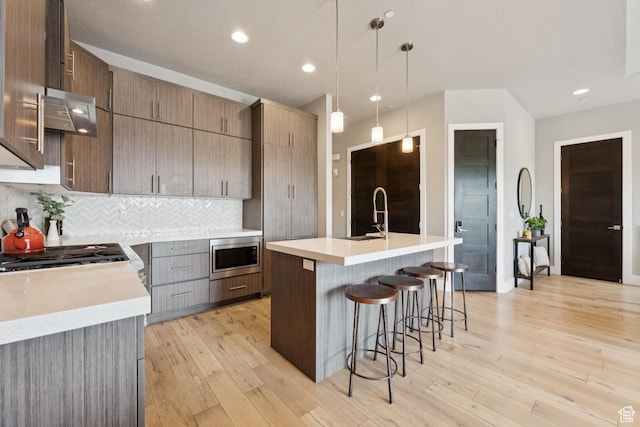 4313 Holly Frost Ct, Park City, UT 84098 - kitchen with stainless steel microwave, light countertops, decorative backsplash, a kitchen bar, and light wood-style floors