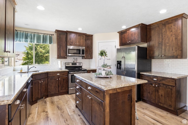 6082 W Cedar Fork Dr S, West Jordan, UT 84081 - kitchen featuring stainless steel appliances, decorative backsplash, a center island, light stone counters, and light wood-style floors