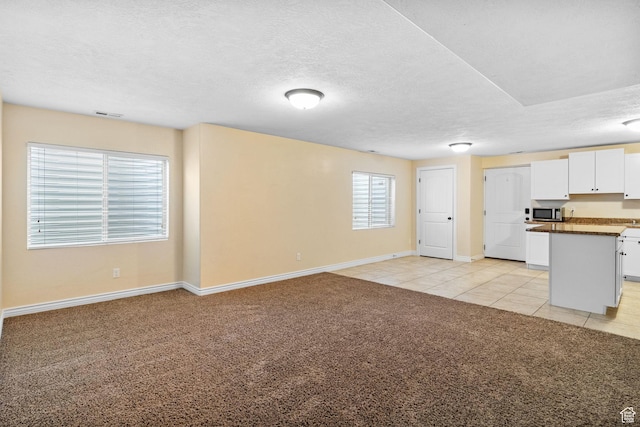 6082 W Cedar Fork Dr S, West Jordan, UT 84081 - kitchen featuring light colored carpet, white cabinetry, stainless steel microwave, dark countertops, and light tile patterned floors