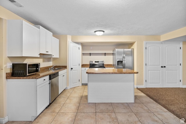 6082 W Cedar Fork Dr S, West Jordan, UT 84081 - kitchen with appliances with stainless steel finishes, white cabinets, a center island, light tile patterned floors, and a textured ceiling