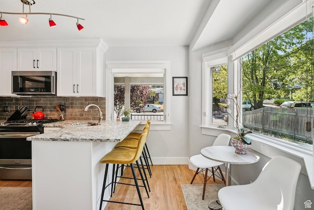 3232 S 2600 E, Salt Lake City, UT 84109 - kitchen with stainless steel appliances, white cabinetry, light stone countertops, tasteful backsplash, and a breakfast bar