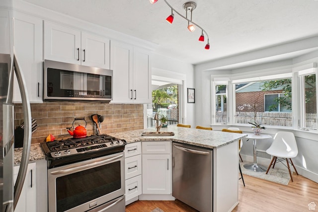 3232 S 2600 E, Salt Lake City, UT 84109 - kitchen with stainless steel appliances, white cabinetry, decorative backsplash, a peninsula, and light wood-type flooring