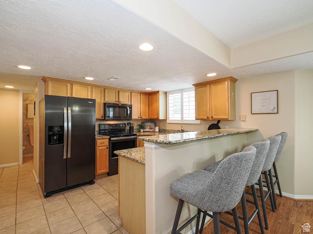 11965 S Draperville Ave, Draper, UT 84020 - kitchen featuring black appliances, recessed lighting, a peninsula, light stone countertops, and a breakfast bar area