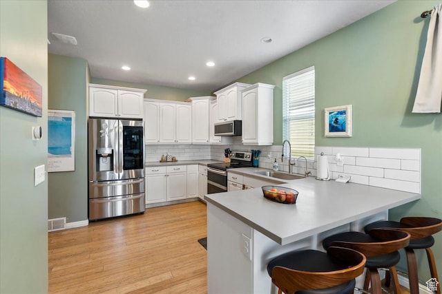 5023 W Currant Dr S, South Jordan, UT 84009 - kitchen with appliances with stainless steel finishes, a peninsula, tasteful backsplash, a kitchen breakfast bar, and white cabinets