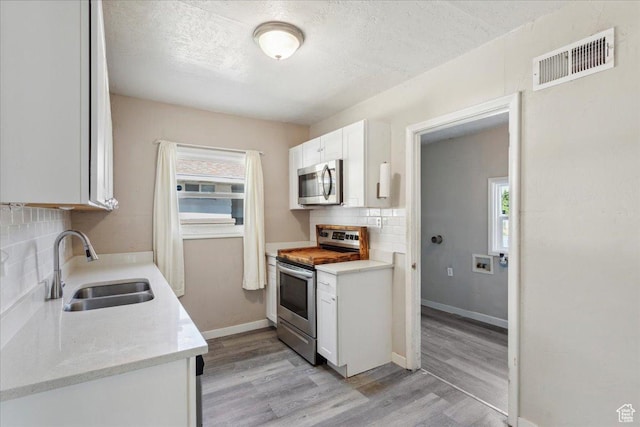 2692 S Monroe Blvd E, Ogden, UT 84401 - kitchen with stainless steel appliances, light wood finished floors, tasteful backsplash, white cabinetry, and a textured ceiling
