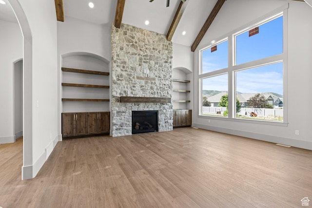 177 E 475 S, Mantua, UT 84324 - unfurnished living room featuring beamed ceiling, high vaulted ceiling, light wood-type flooring, arched walkways, and a stone fireplace