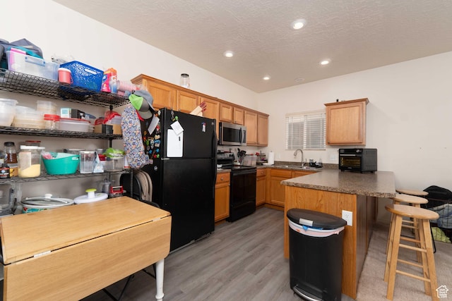 392 E 700 S Unit H, Vernal, UT 84078 - kitchen featuring black appliances, a peninsula, light wood finished floors, a breakfast bar area, and a textured ceiling