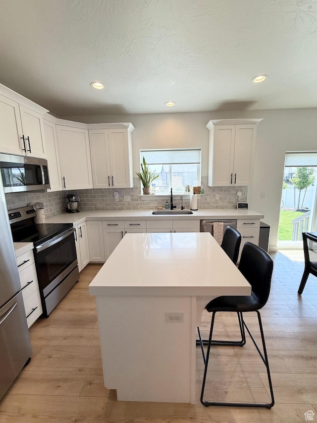 1258 E Bell Buoy Way, Eagle Mountain, UT 84005 - kitchen with stainless steel appliances, a kitchen bar, decorative backsplash, light countertops, and light wood-type flooring