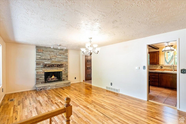 6690 S 1495 E, Cottonwood Heights, UT 84121 - unfurnished living room featuring a textured ceiling, light wood-style flooring, a chandelier, and a stone fireplace