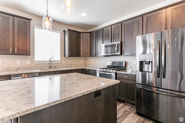 4567 W Breezy Meadow Dr, Herriman, UT 84096 - kitchen featuring stainless steel appliances, dark brown cabinets, light wood-type flooring, light stone countertops, and pendant lighting