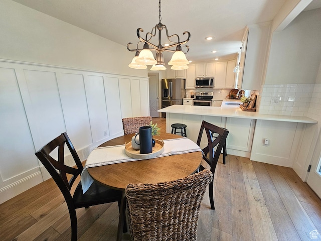 3501 E Golden Eagle Rd N, Eagle Mountain, UT 84005 - dining space with light wood-style floors, a chandelier, a decorative wall, recessed lighting, and wainscoting