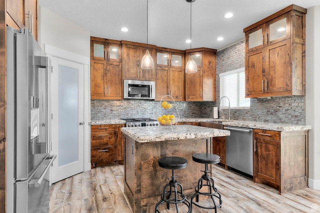 13703 S Blayde Dr, Herriman, UT 84096 - kitchen featuring appliances with stainless steel finishes, light wood-style floors, a center island, brown cabinetry, and tasteful backsplash