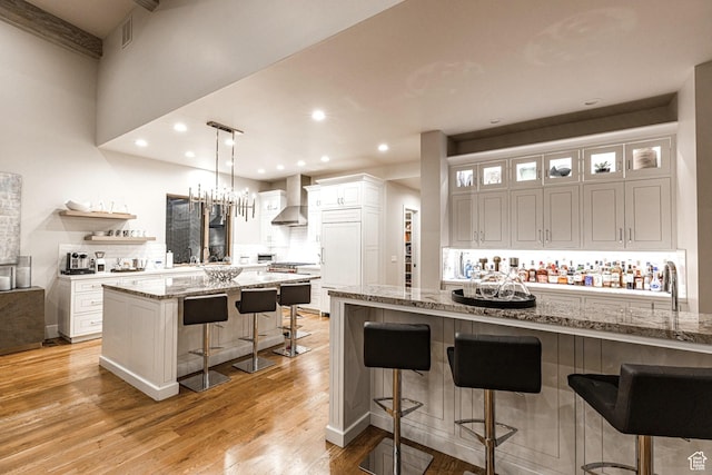 6423 Golden Bear Loop Unit 5, Park City, UT 84098 - kitchen with wall chimney exhaust hood, a kitchen bar, white cabinetry, light wood-style floors, and light stone counters