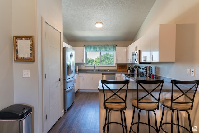 618 S 100th St W # D302, Springville, UT 84663 - kitchen featuring appliances with stainless steel finishes, a peninsula, dark countertops, a textured ceiling, and a kitchen breakfast bar