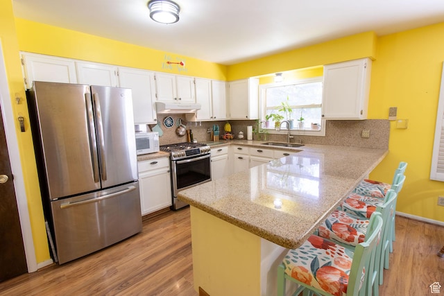 1471 W Stern Dr S, Taylorsville, UT 84123 - kitchen with stainless steel appliances, under cabinet range hood, a peninsula, white cabinetry, and light wood-style floors
