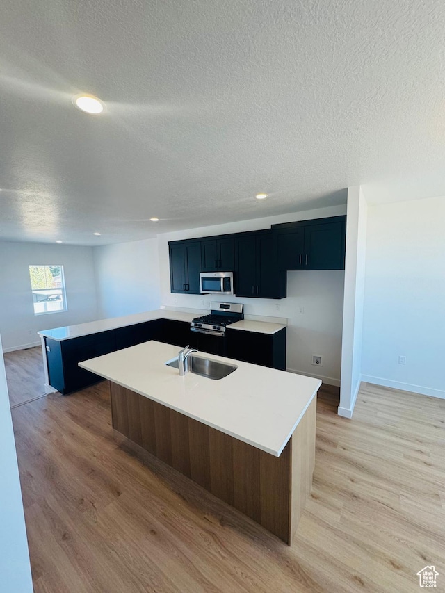 1650 N Main St Unit 126, Layton, UT 84041 - kitchen featuring appliances with stainless steel finishes, a center island with sink, light wood-type flooring, a textured ceiling, and light countertops