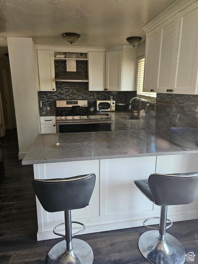 3243 S Fairlane St, Magna, UT 84044 - kitchen featuring wall chimney exhaust hood, gas stove, a peninsula, white cabinets, and tasteful backsplash