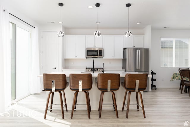 6392 N Wild Mare Way, Stansbury Park, UT 84074 - kitchen with stainless steel appliances, light wood-style flooring, a kitchen island with sink, white cabinetry, and decorative light fixtures