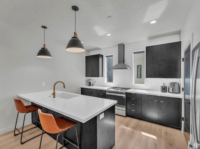 351 W 800 N # 9, Salt Lake City, UT 84103 - kitchen featuring wall chimney range hood, appliances with stainless steel finishes, dark cabinetry, light countertops, and a breakfast bar