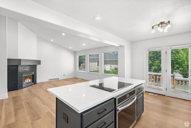 713 S 600 E, Layton, UT 84041 - kitchen with oven, black electric stovetop, light wood-style flooring, gray cabinets, and a glass covered fireplace