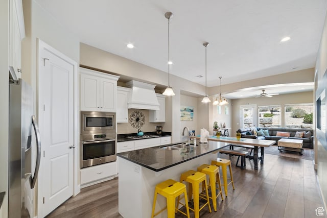 2076 N Doral Ct, Washington, UT 84780 - kitchen featuring appliances with stainless steel finishes, custom exhaust hood, dark countertops, open floor plan, and dark wood-style flooring