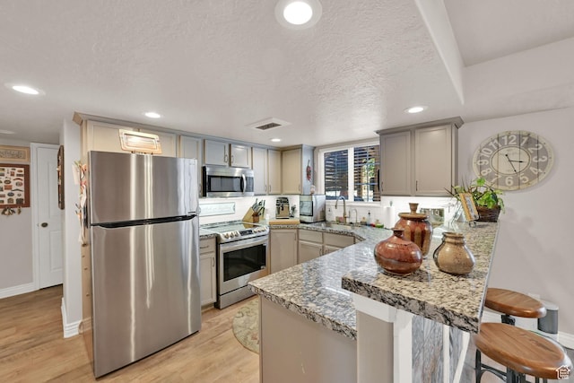 11999 S Draperville Ave, Draper, UT 84020 - kitchen with stainless steel appliances, a peninsula, a kitchen breakfast bar, light wood-style floors, and a textured ceiling