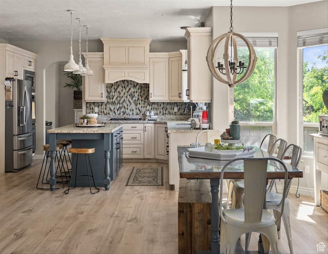 3371 W Waterbridge Cv Unit 417, South Jordan, UT 84095 - kitchen with appliances with stainless steel finishes, a chandelier, a breakfast bar, decorative backsplash, and light wood finished floors
