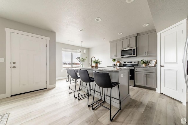 2259 S 1180 W Unit 12, Nibley, UT 84321 - kitchen with stainless steel appliances, gray cabinetry, light stone counters, a breakfast bar, and light wood-style floors