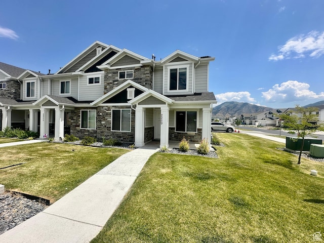 2259 S 1180 W Unit 12, Nibley, UT 84321 - view of front of property featuring stone siding, a front yard, a mountain view, and covered porch