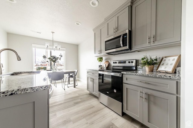2259 S 1180 W Unit 12, Nibley, UT 84321 - kitchen featuring appliances with stainless steel finishes, gray cabinetry, light wood-style floors, light stone counters, and a textured ceiling