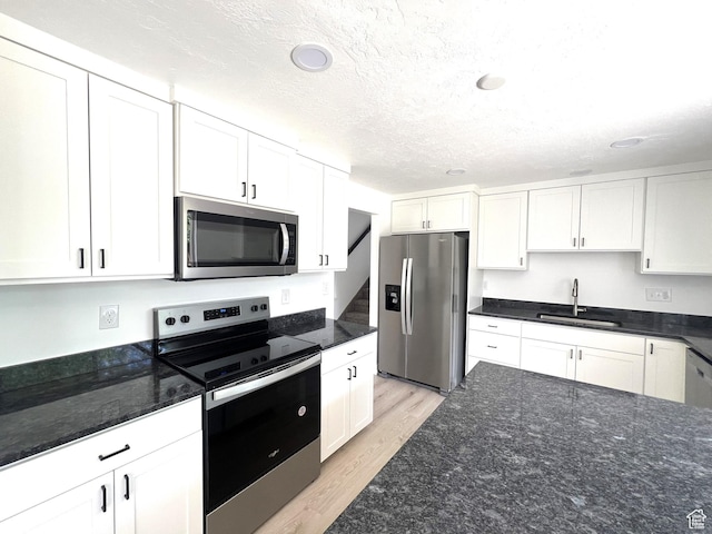 686 N Parkway Ave, Tooele, UT 84074 - kitchen with stainless steel appliances, light wood finished floors, white cabinets, dark stone counters, and a textured ceiling