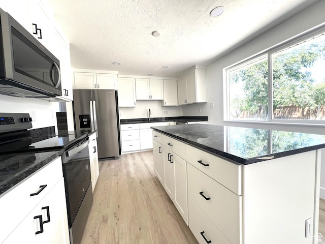 686 N Parkway Ave, Tooele, UT 84074 - kitchen with appliances with stainless steel finishes, light wood-style flooring, a textured ceiling, white cabinetry, and a center island