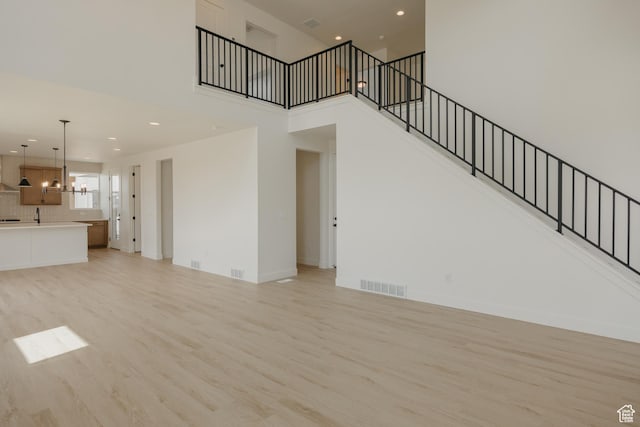 1026 W Chokecherry Dr Unit 135, Mapleton, UT 84664 - unfurnished living room with light wood finished floors, a chandelier, a high ceiling, stairs, and recessed lighting