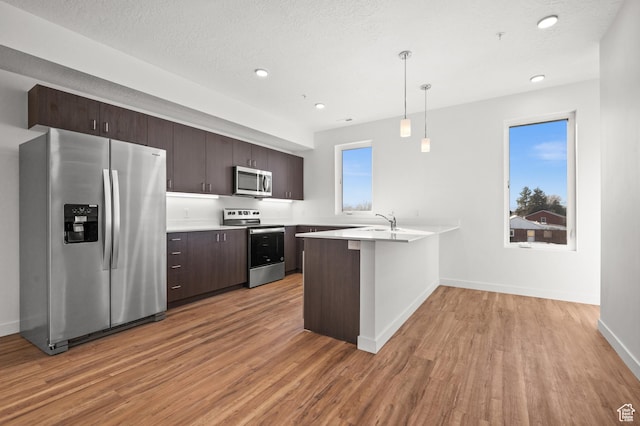 1034 W 1700 S Unit 124, Salt Lake City, UT 84104 - kitchen with stainless steel appliances, a peninsula, dark brown cabinetry, light wood-style floors, and light countertops