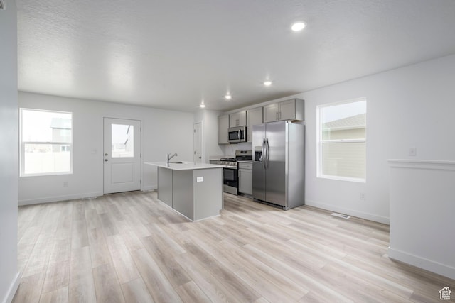 1857 E Bison Dr Unit B217, Eagle Mountain, UT 84005 - kitchen featuring appliances with stainless steel finishes, gray cabinets, light countertops, a kitchen island with sink, and light wood-type flooring