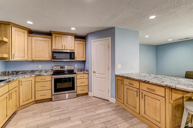 709 N 2200 E, St George, UT 84790 - kitchen with appliances with stainless steel finishes, wood tiled floors, light stone counters, light brown cabinetry, and a textured ceiling