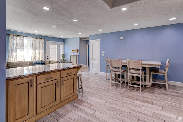 709 N 2200 E, St George, UT 84790 - kitchen featuring a textured ceiling, light wood finished floors, open floor plan, a kitchen bar, and light stone countertops