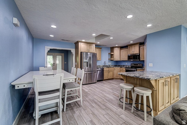 709 N 2200 E, St George, UT 84790 - kitchen featuring appliances with stainless steel finishes, light wood-style flooring, a peninsula, a textured ceiling, and a kitchen breakfast bar