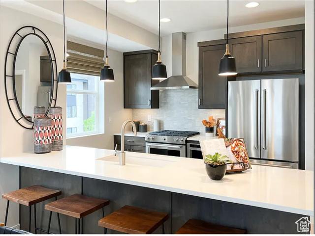 6785 Silver Creek Dr N, Park City, UT 84098 - kitchen with stainless steel appliances, wall chimney range hood, decorative backsplash, decorative light fixtures, and a kitchen breakfast bar