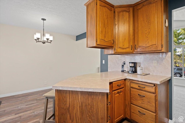 7351 W Zana Ln, Magna, UT 84044 - kitchen with brown cabinetry, light wood-style flooring, light countertops, backsplash, and a chandelier