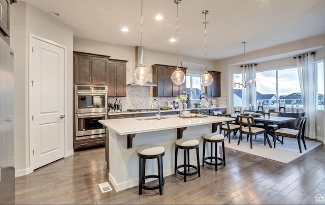 6258 W Teton Ranch Dr S Unit 309, Herriman, UT 84096 - kitchen featuring stainless steel appliances, wall chimney exhaust hood, a breakfast bar, light countertops, and decorative backsplash